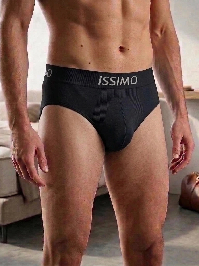 A man wearing black Issimo men's briefs, shown from the waist down in a softly lit indoor setting.